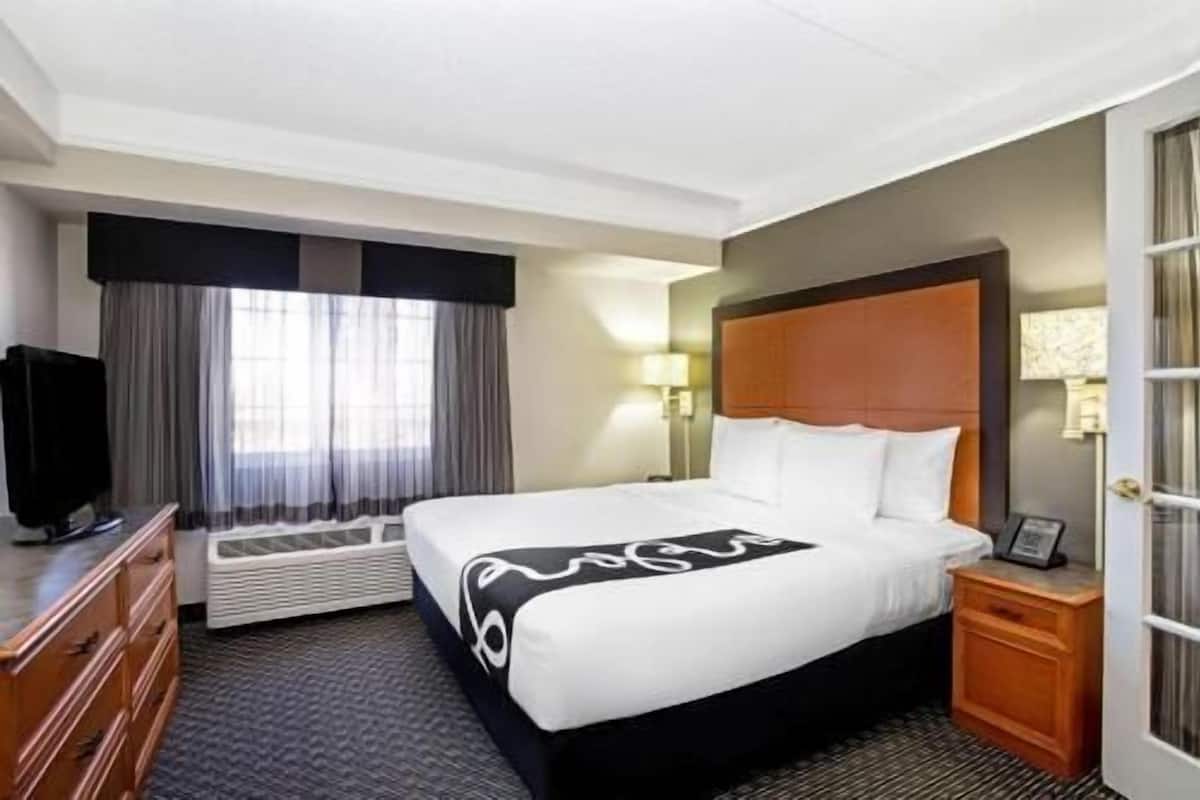 A hotel room with a bed, a television, a desk, a lamp, and a door.