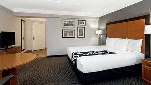 Una habitación de hotel con cama, escritorio, televisor y cuadros en la pared.