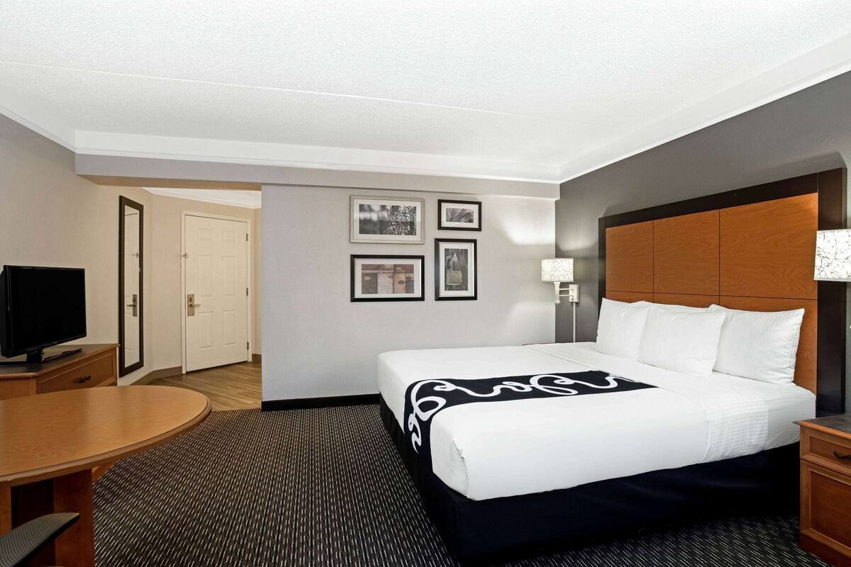 A hotel room with a bed, a desk, a television, and framed pictures on the wall.