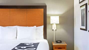 Ein Hotelzimmer mit Holzkopfteil, einem Bett mit weißer Bettwäsche, einem Nachttisch mit Lampe und einem gerahmten Bild an der Wand.