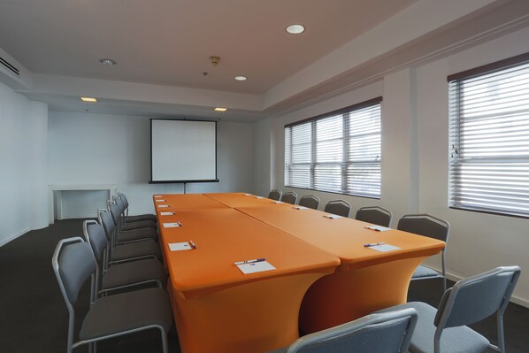 A conference room with a long table, chairs, a projector screen, and windows with blinds.