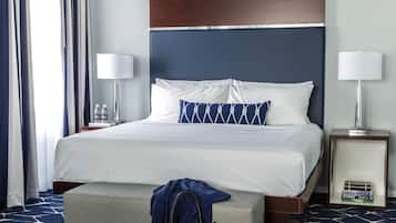 Une chambre d’hôtel avec un grand lit, une table de chevet avec une lampe, une commode avec une lampe, une fenêtre avec des rideaux et un tapis à motifs.