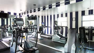A gym with various exercise machines, including treadmills and weight benches, and a mirrored wall reflecting the equipment.