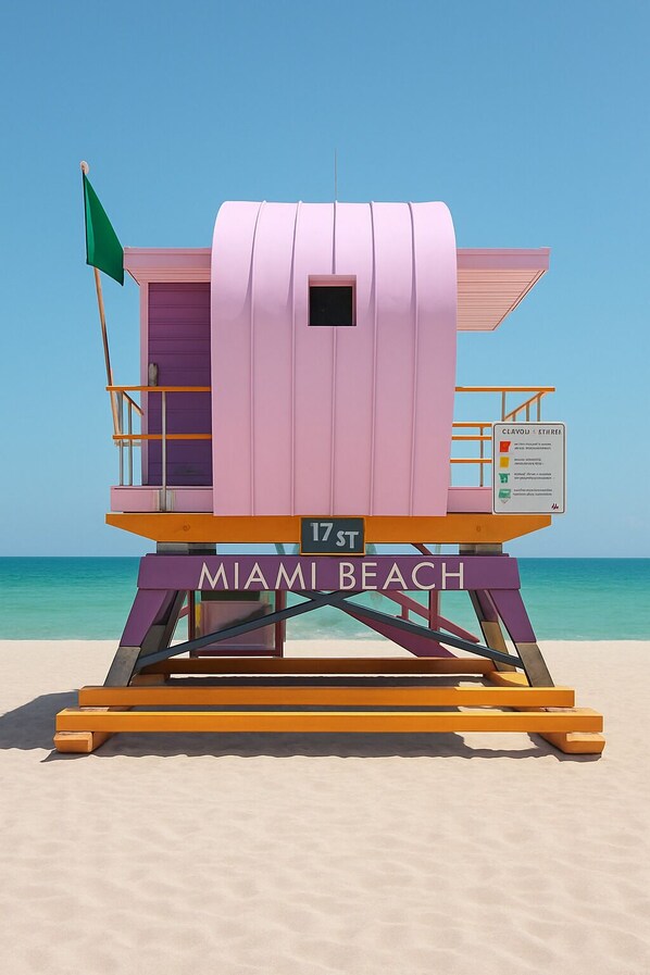 A lifeguard tower at Miami Beach with a flag, a sign indicating the address, and the name 'MIAMI BEACH' on the base.