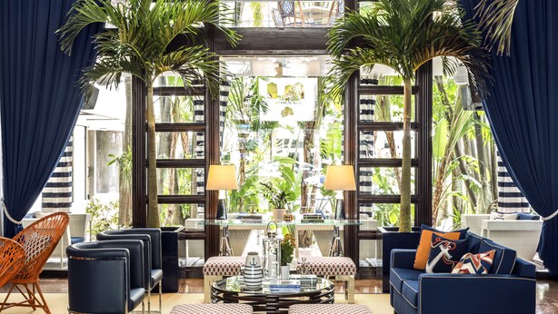 A spacious living room with a large glass window, a blue sofa, a patterned ottoman, and a wicker chair. - Albion South Beach Hotel (Miami Beach)