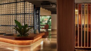 A modern reception area with a wooden reception desk, a large potted plant, and a seating area with chairs. - The Gates Hotel South Beach (Miami Beach)