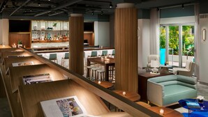 A modern bar area with a long counter, bar stools, and a seating area with a sofa and chairs. - The Gates Hotel South Beach (Miami Beach)