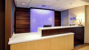 Un comptoir d’accueil d’hôtel avec un comptoir en bois, un mur bleu éclairé et un panneau indiquant qu’il est interdit d’y faire entrer des animaux de compagnie.