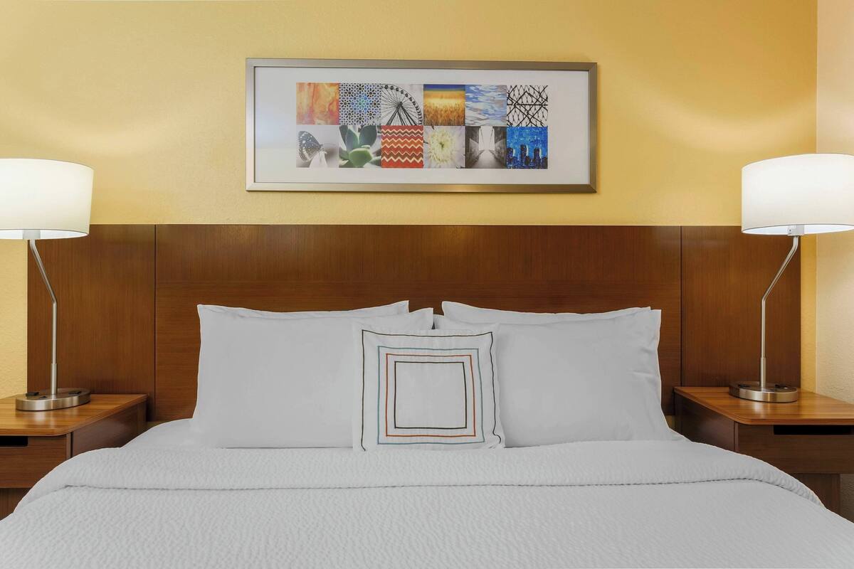 Una cama bien hecha con sábanas blancas y una obra enmarcada encima.