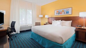 Une chambre d’hôtel avec un grand lit, un bureau avec un ordinateur, une chaise, une télévision et une fenêtre avec des rideaux.