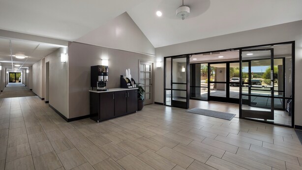 A modern hotel lobby with a reception desk, a large glass door leading outside, and a long corridor with a ceiling light. - Red Roof Inn Tucson North - Marana (Tucson)