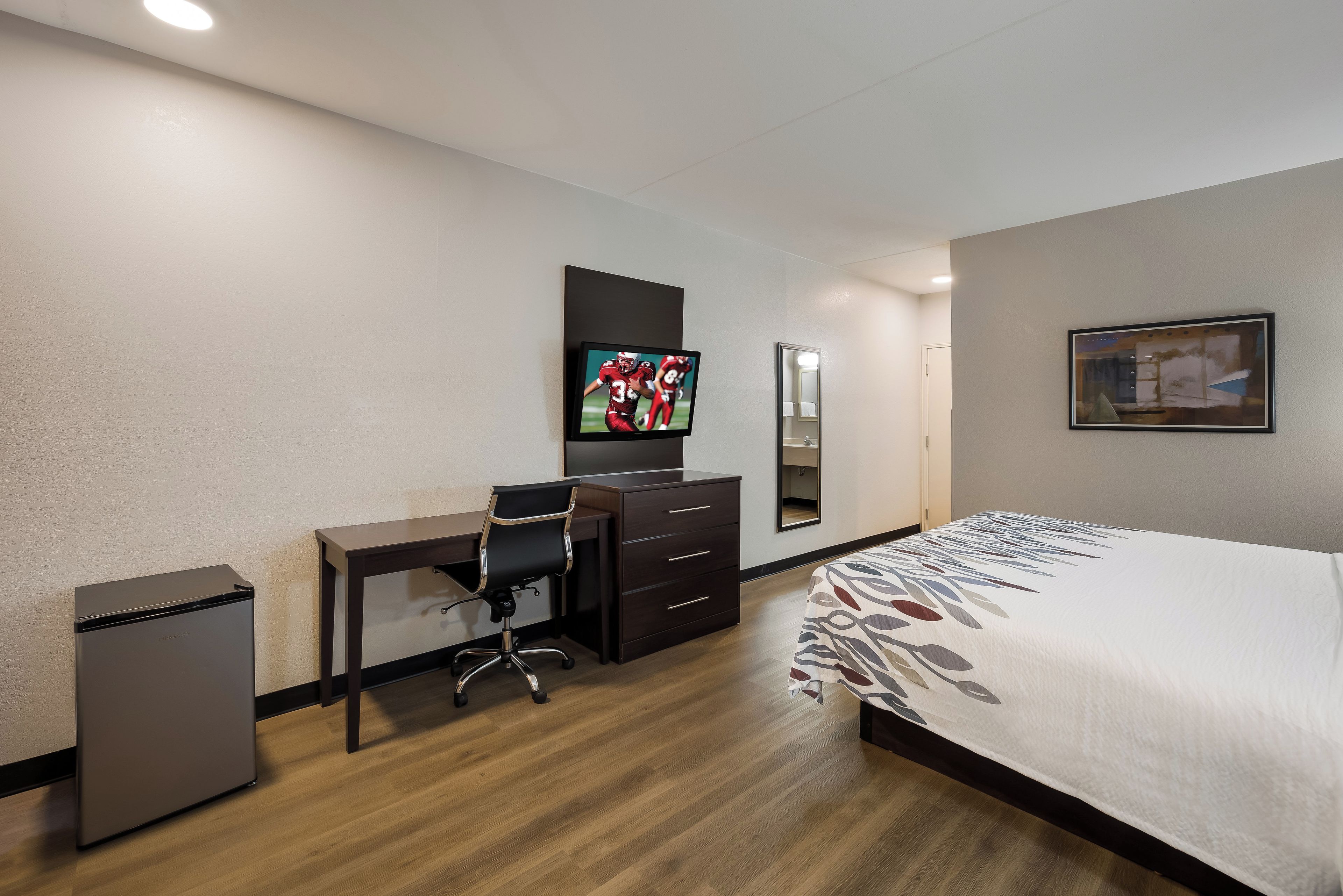 A hotel room with a bed, a desk, a chair, a television, a dresser, and a mirror.