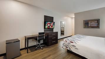 A hotel room with a bed, a desk, a chair, a television, a dresser, and a mirror.