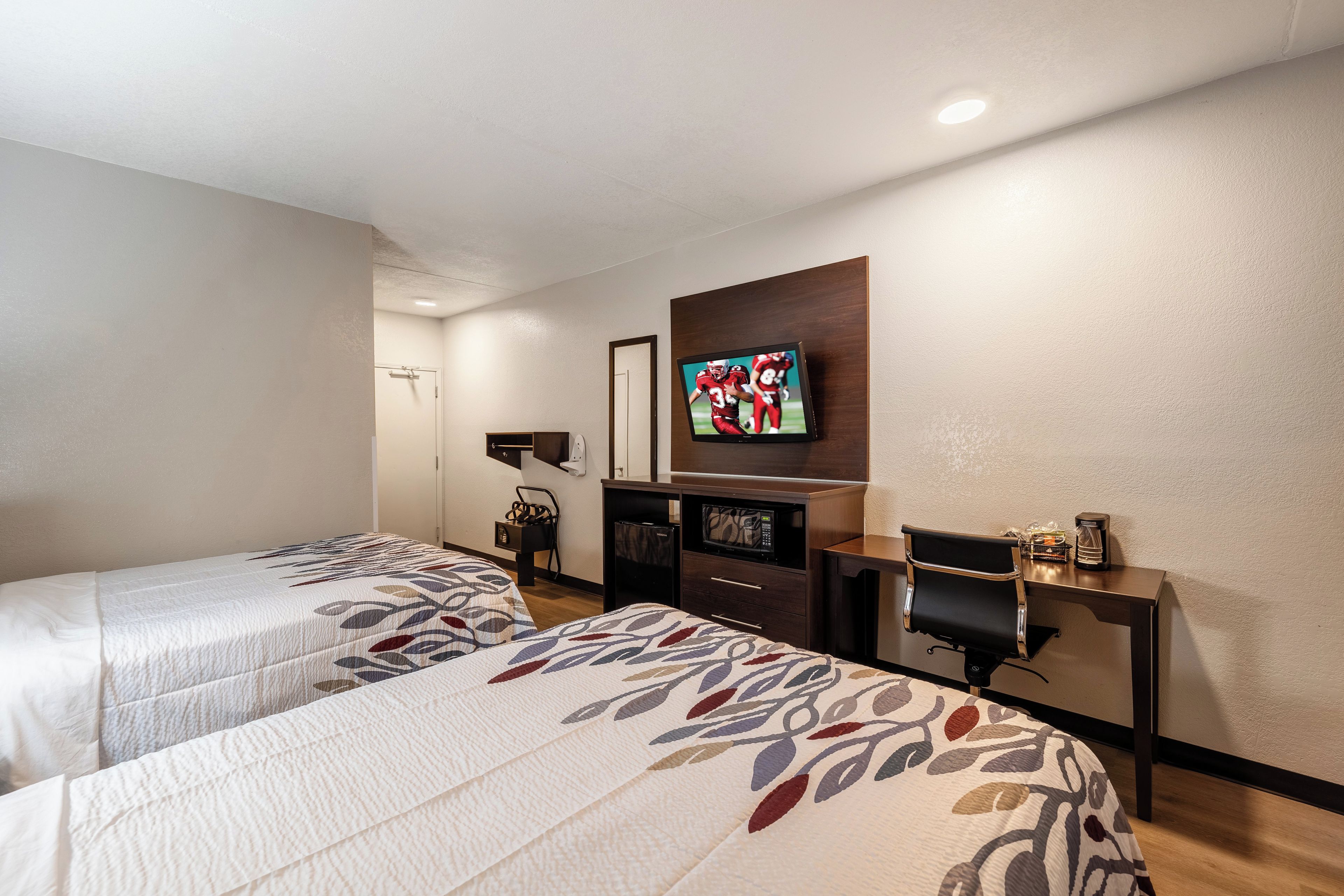 A hotel room with two beds, a television, a desk, and a microwave.