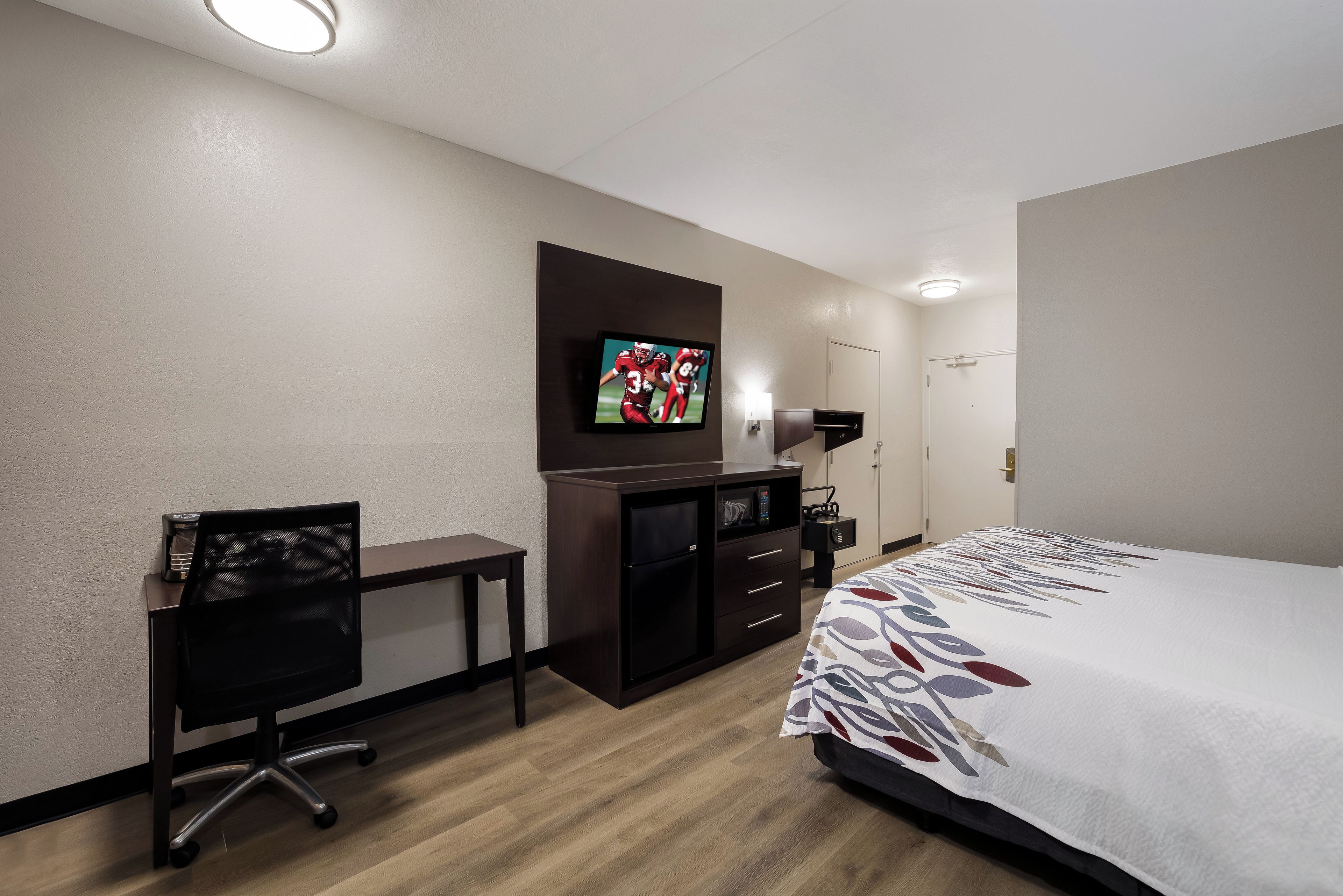 A hotel room with a bed, a desk, a chair, a TV, a wardrobe, and a bedside table.
