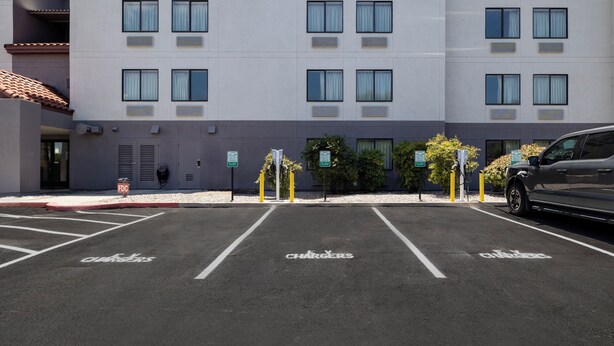 Ein Parkplatz mit Ladestationen für Elektrofahrzeuge, ausgewiesenen Stellplätzen und einem Gebäude mit zahlreichen Fenstern und Klimaanlagen.
