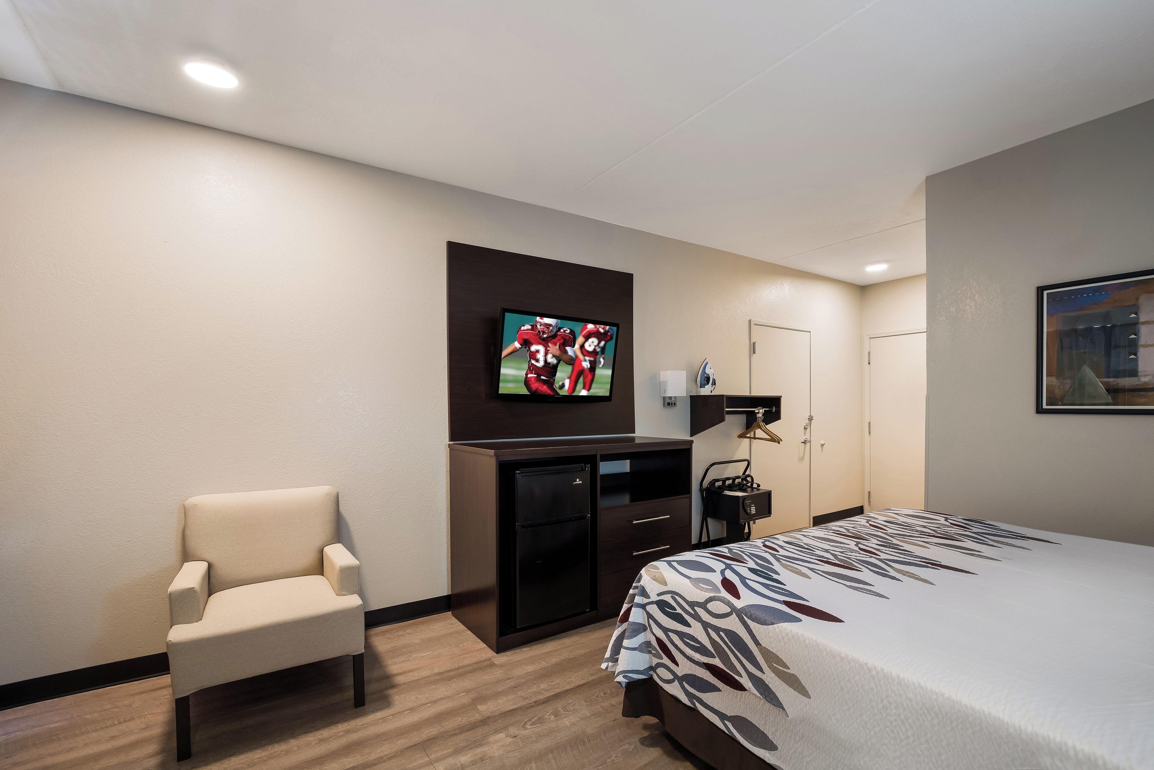 Una habitación de hotel con cama, escritorio, silla, televisor y armario.