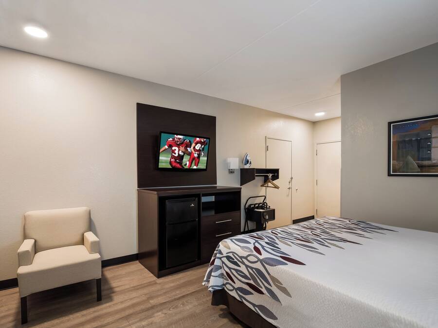 Una habitación de hotel con cama, escritorio, silla, televisor y armario.