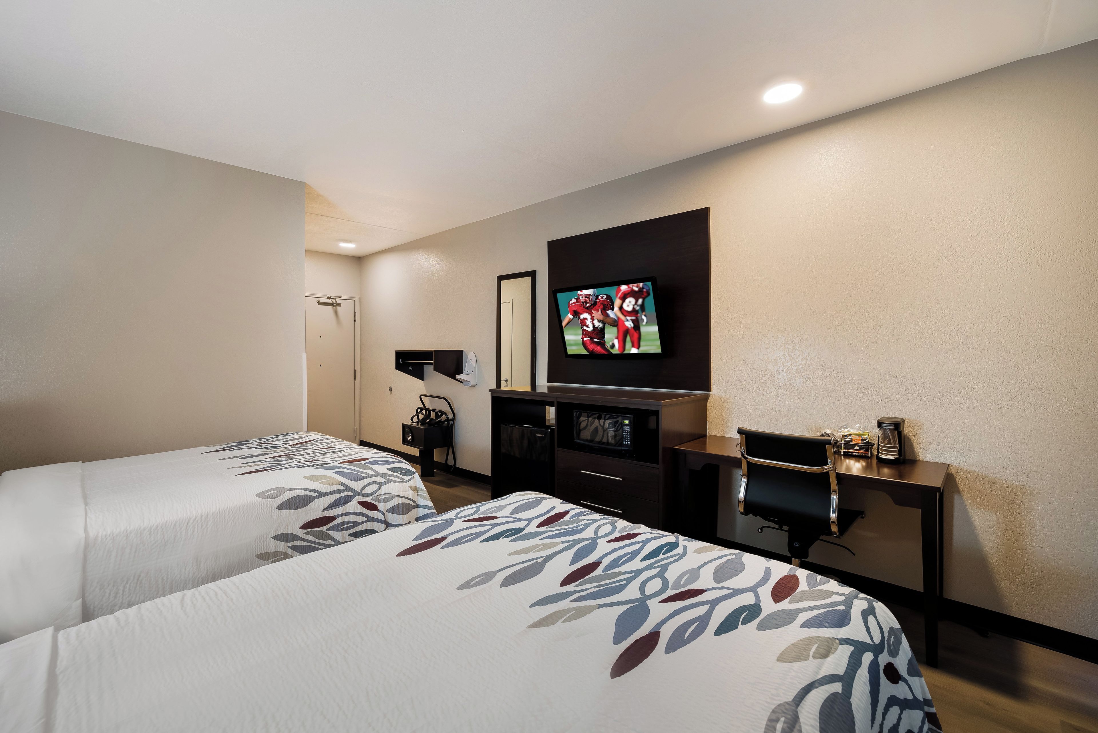 Habitación de hotel con dos camas, un televisor montado en la pared, un escritorio con una silla y un perchero.