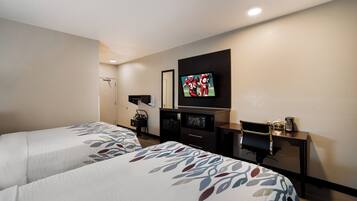 Une chambre d’hôtel avec deux lits, un téléviseur fixé au mur, un bureau avec une chaise et un porte-manteau.