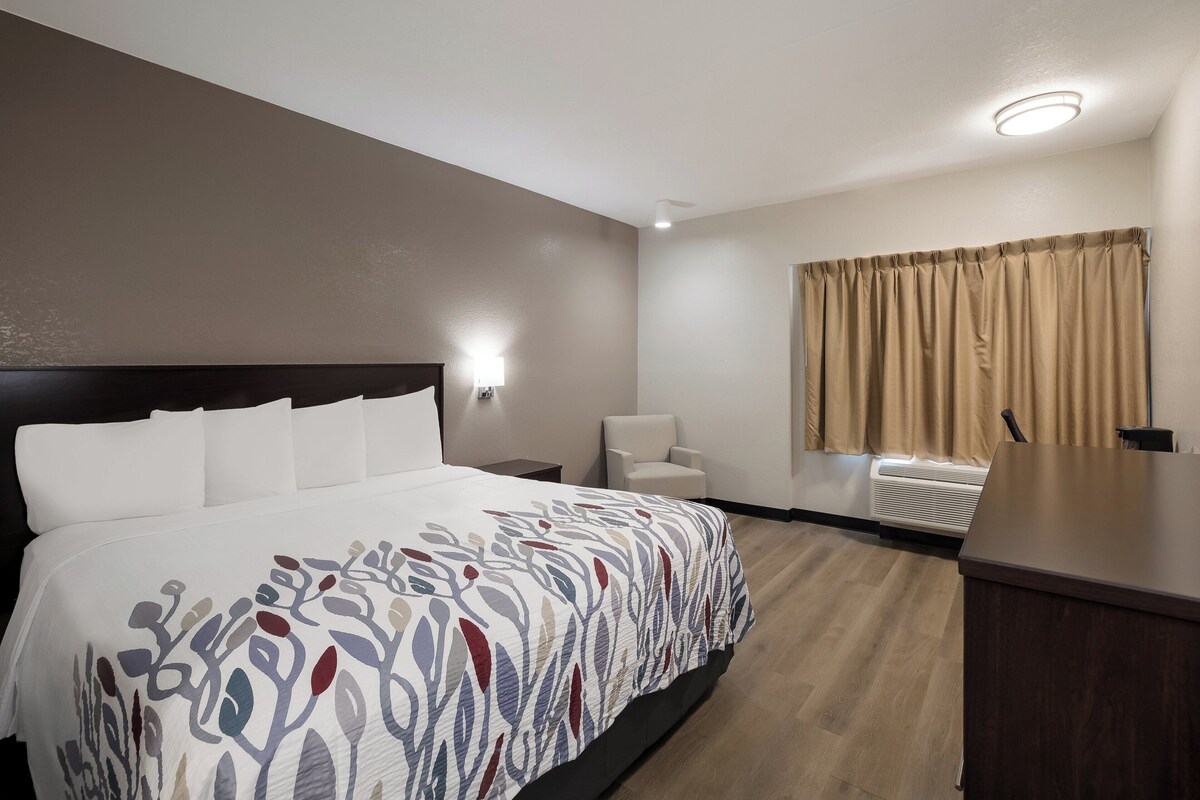 A hotel room with a large bed, a chair, a desk, and a window with curtains.