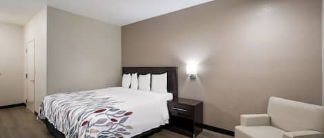 A hotel room with a bed, a nightstand, a chair, and a wall-mounted light.