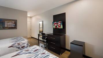 A hotel room with two beds, a desk, a chair, a television, and a small refrigerator.
