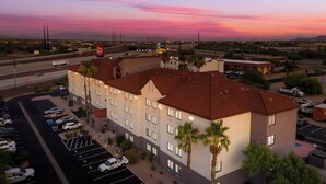 A multi-story hotel with a parking lot, a red-roofed building, and a view of the surrounding area during sunset. - Red Roof Inn Tucson North - Marana (Tucson)