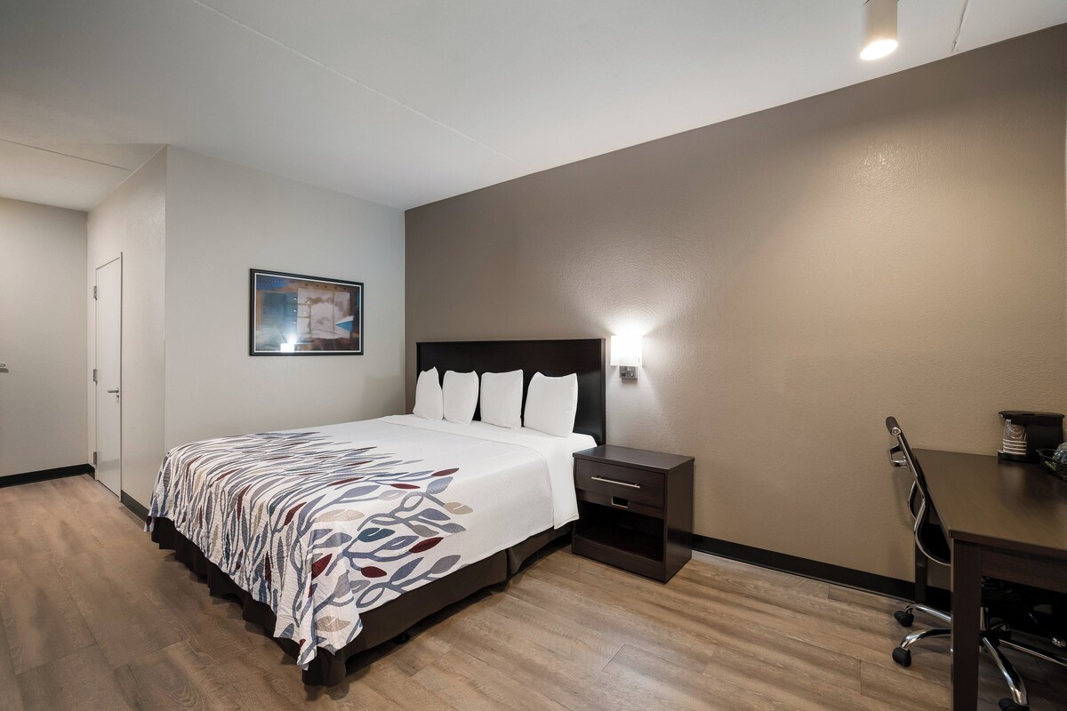 A hotel room with a bed, bedside table, desk, and chair.