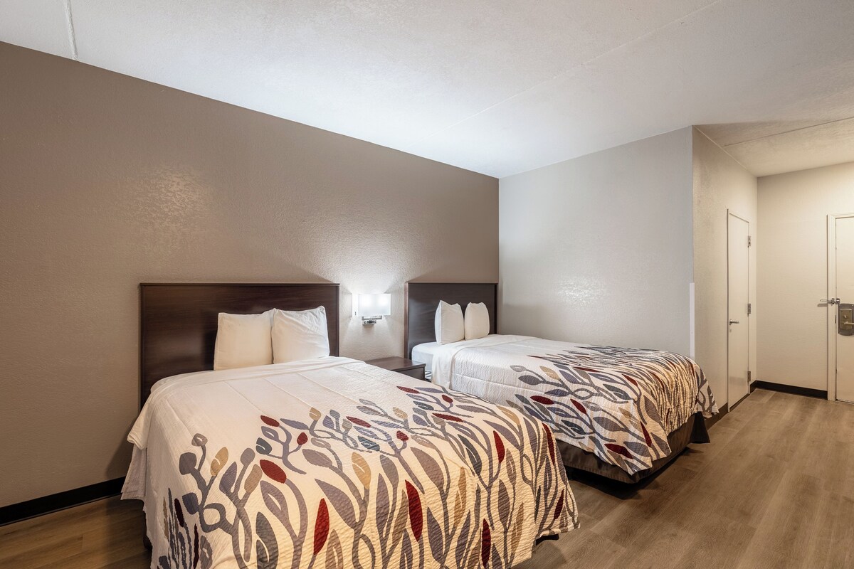 A hotel room with two beds, wooden headboards, and a light-colored wall.