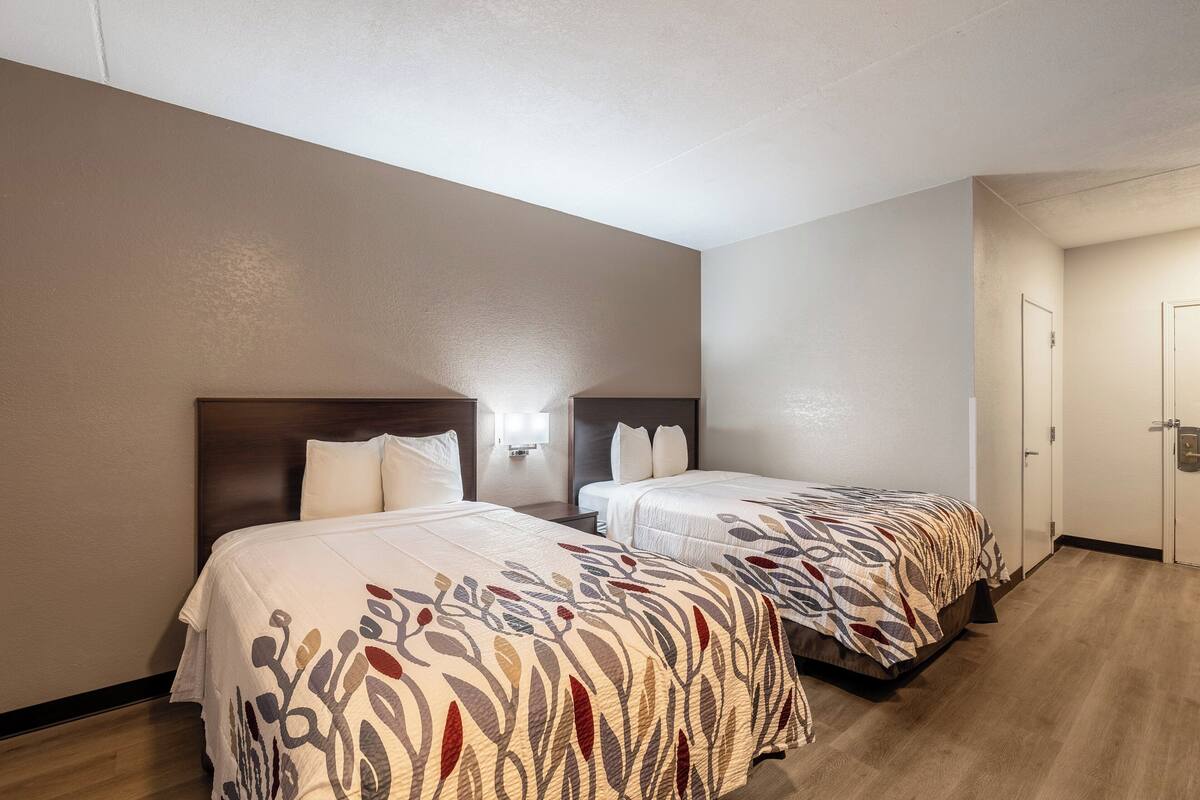 Habitación de hotel con dos camas, cabeceros de madera y pared de color claro.