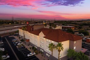 A multi-story hotel with a parking lot, a red-roofed building, and a view of the surrounding area during sunset. - Red Roof Inn Tucson North - Marana (Tucson)