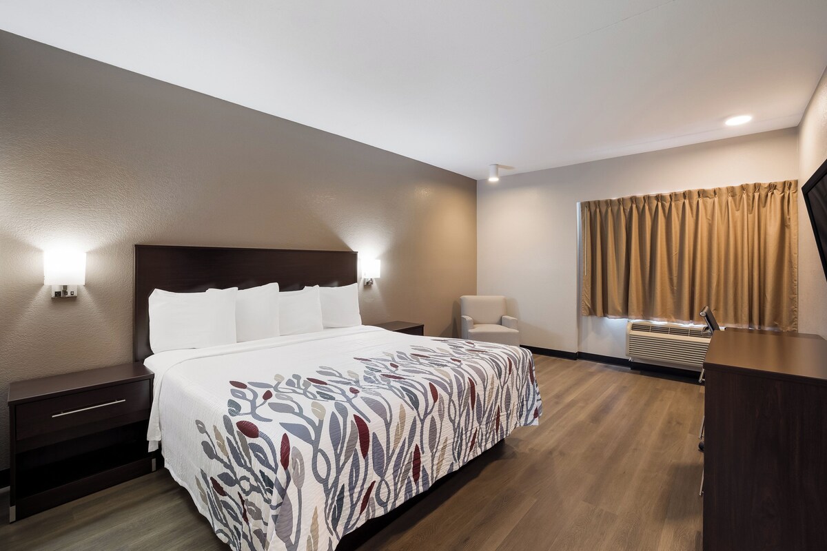 A hotel room with a large bed, bedside lamps, a chair, a desk, and a window with curtains.