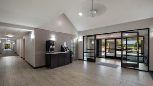 Eine moderne Hotelhalle mit einer Rezeption, einer Kaffeemaschine und einer großen Glastür, die zu einem Außenbereich führt.