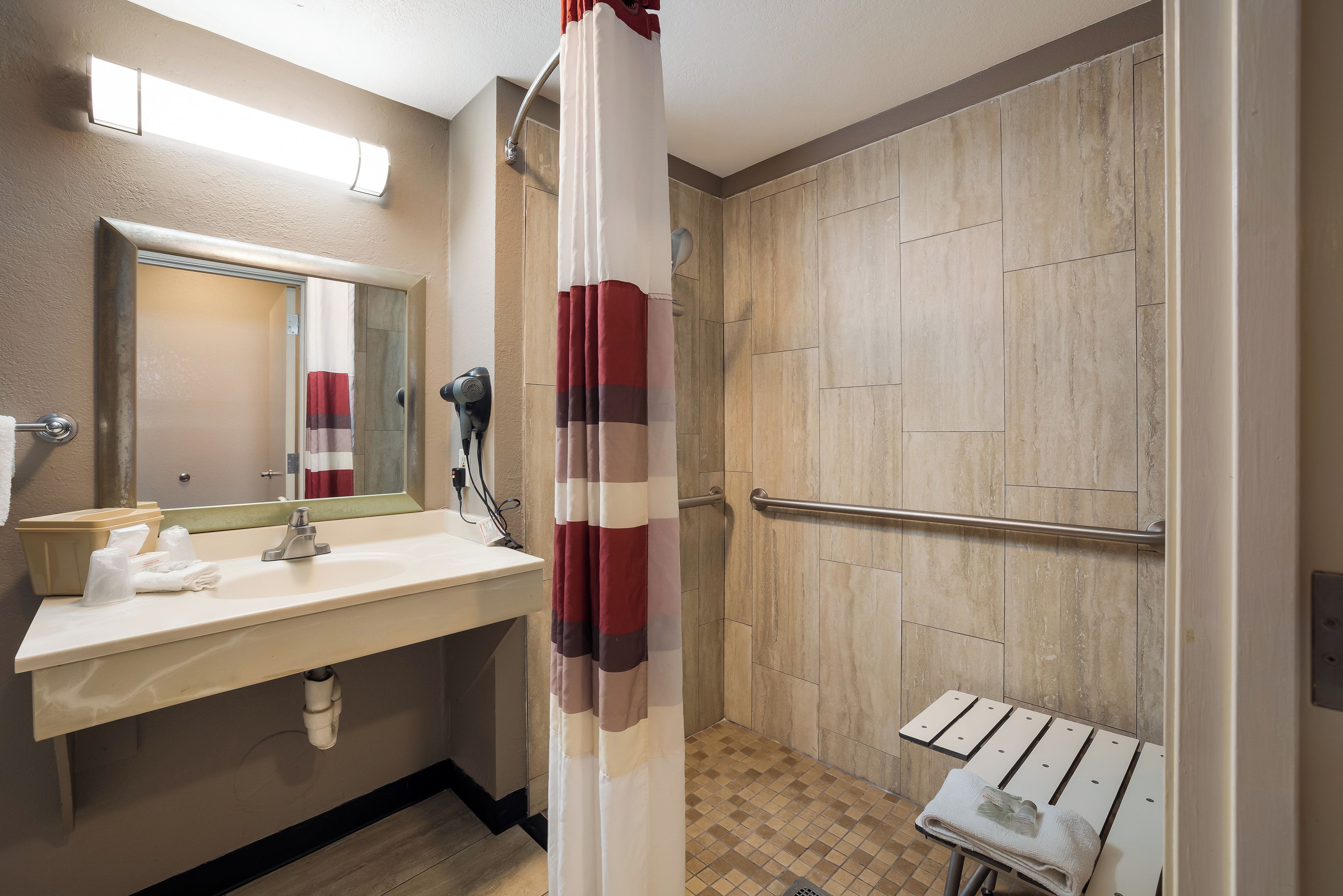 A bathroom with a sink, mirror, towel rack, shower curtain, and a small table with a towel.