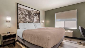 Une chambre d’hôtel moderne, dotée d’un grand lit, d’une table de chevet, d’une lampe fixée au mur et d’une fenêtre offrant une vue agréable.