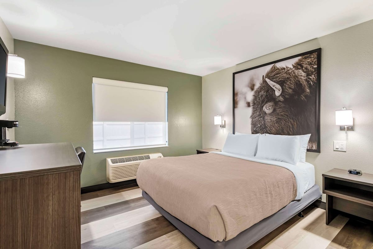 Ein Hotelzimmer mit einem Bett, einem Nachttisch, einer Lampe und einem großen gerahmten Bild an der Wand.