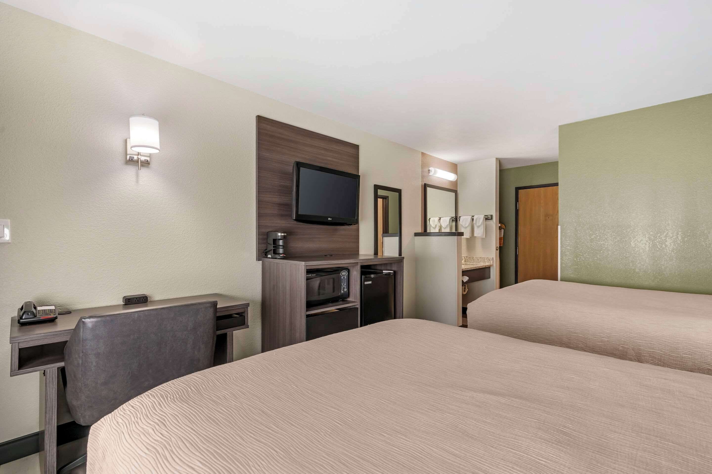 Une chambre d’hôtel avec deux lits, un bureau avec une chaise, une télévision, un four à micro-ondes et un petit réfrigérateur.