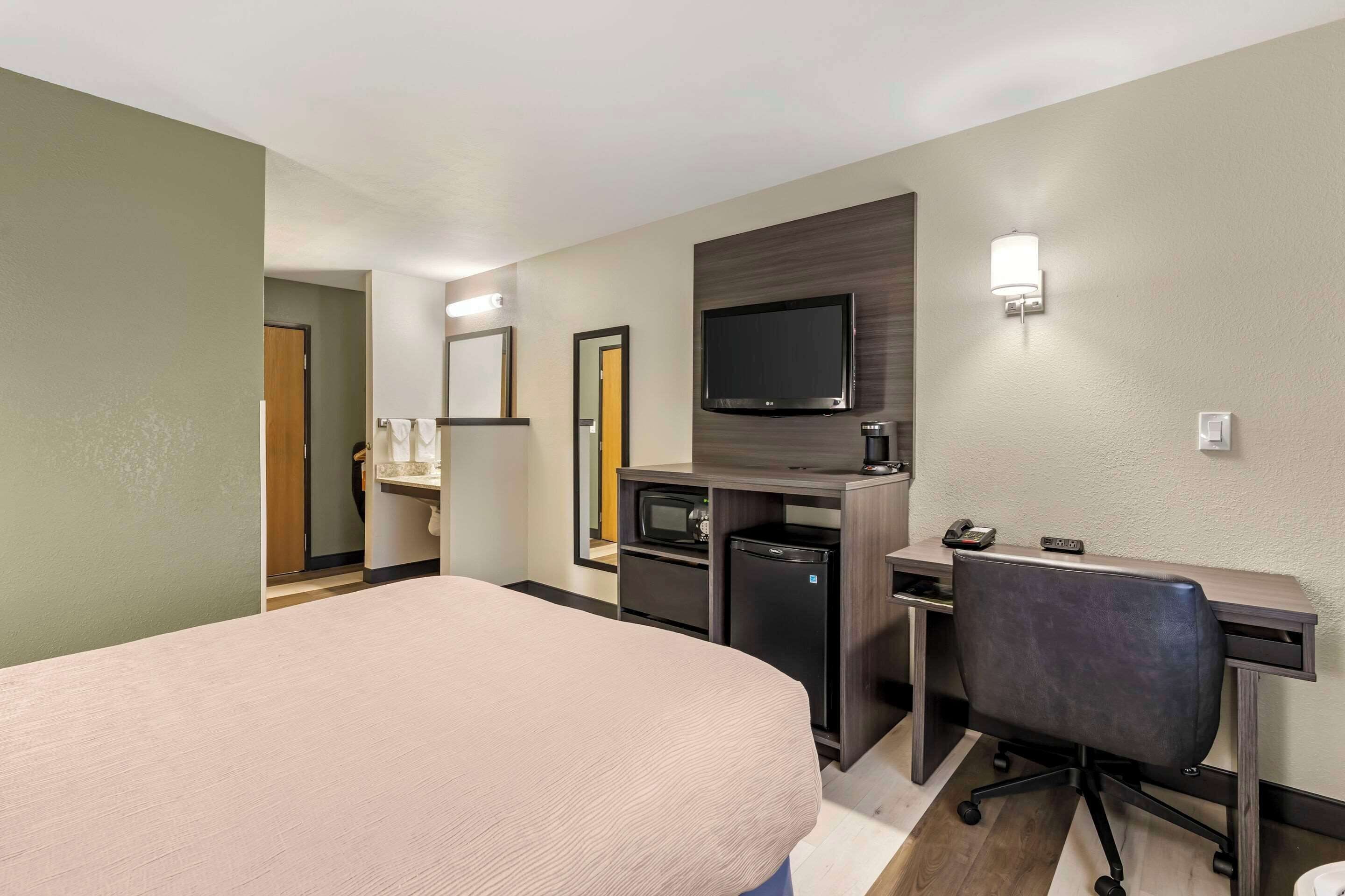 A hotel room with a bed, desk, chair, television, and a microwave.