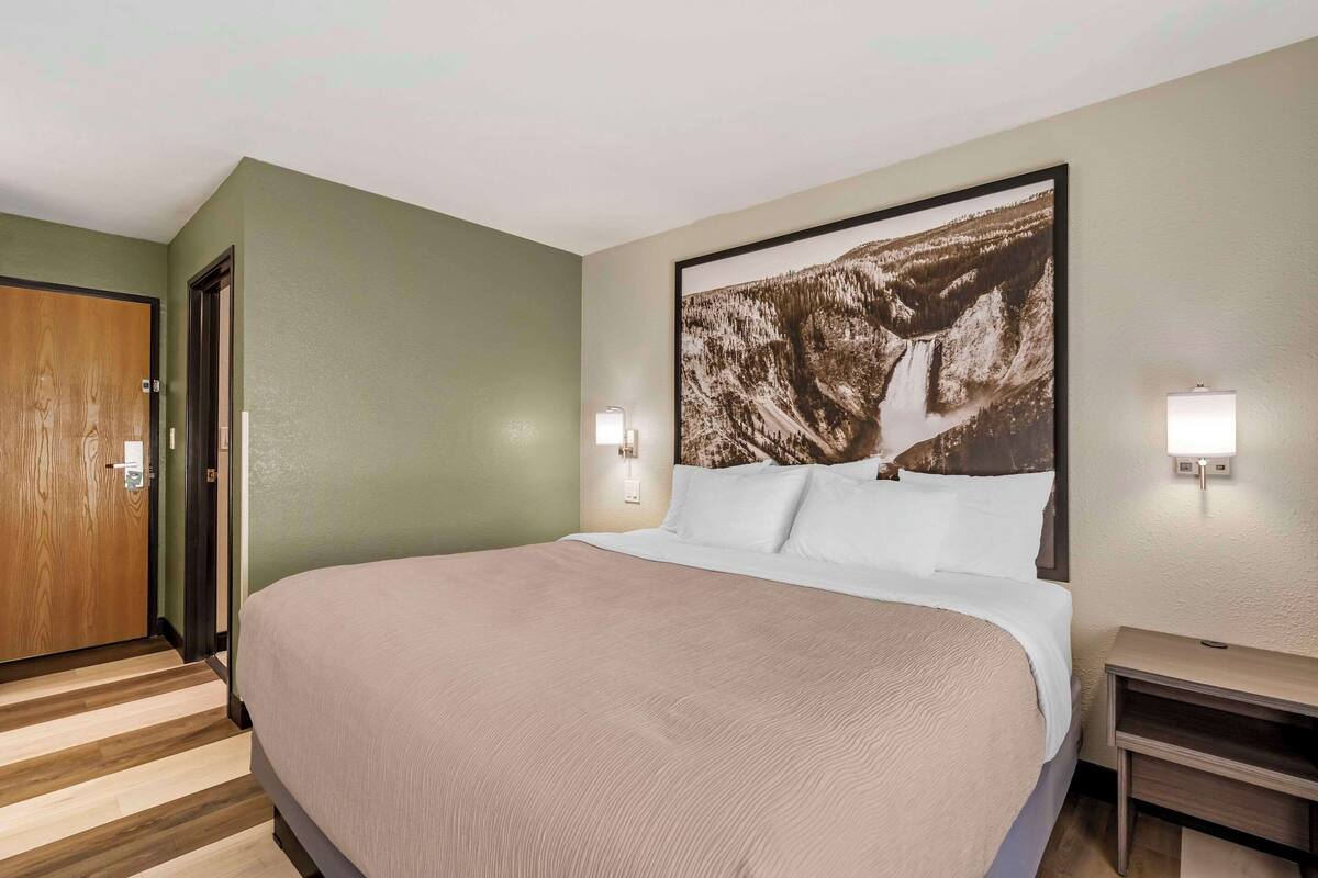 Ein Hotelzimmer mit einem großen Bett, einer Holztür, einem Wandbild und einem Nachttisch.