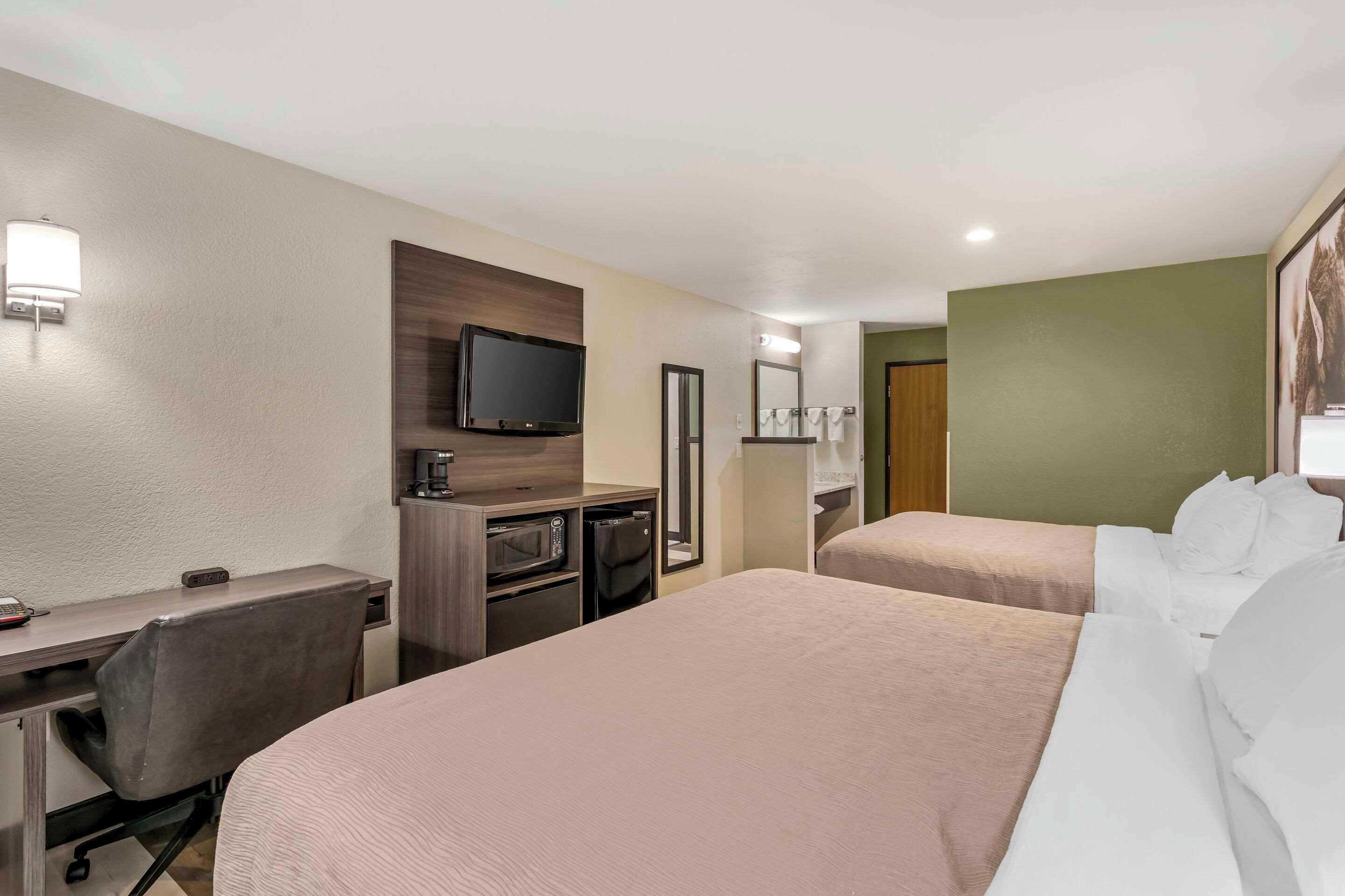A hotel room with two beds, a desk with a chair, a television, a coffee machine, and a microwave.