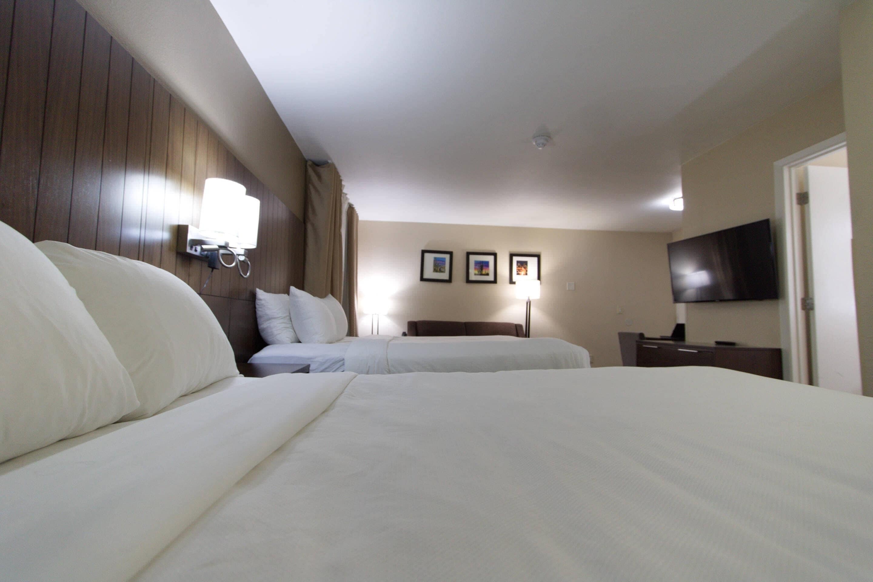 A hotel room with two beds, a flat-screen TV, a bedside table, and a wall-mounted lamp.