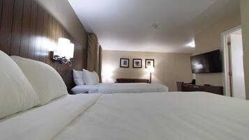 A hotel room with two beds, a flat-screen TV, a bedside table, and a wall-mounted lamp.