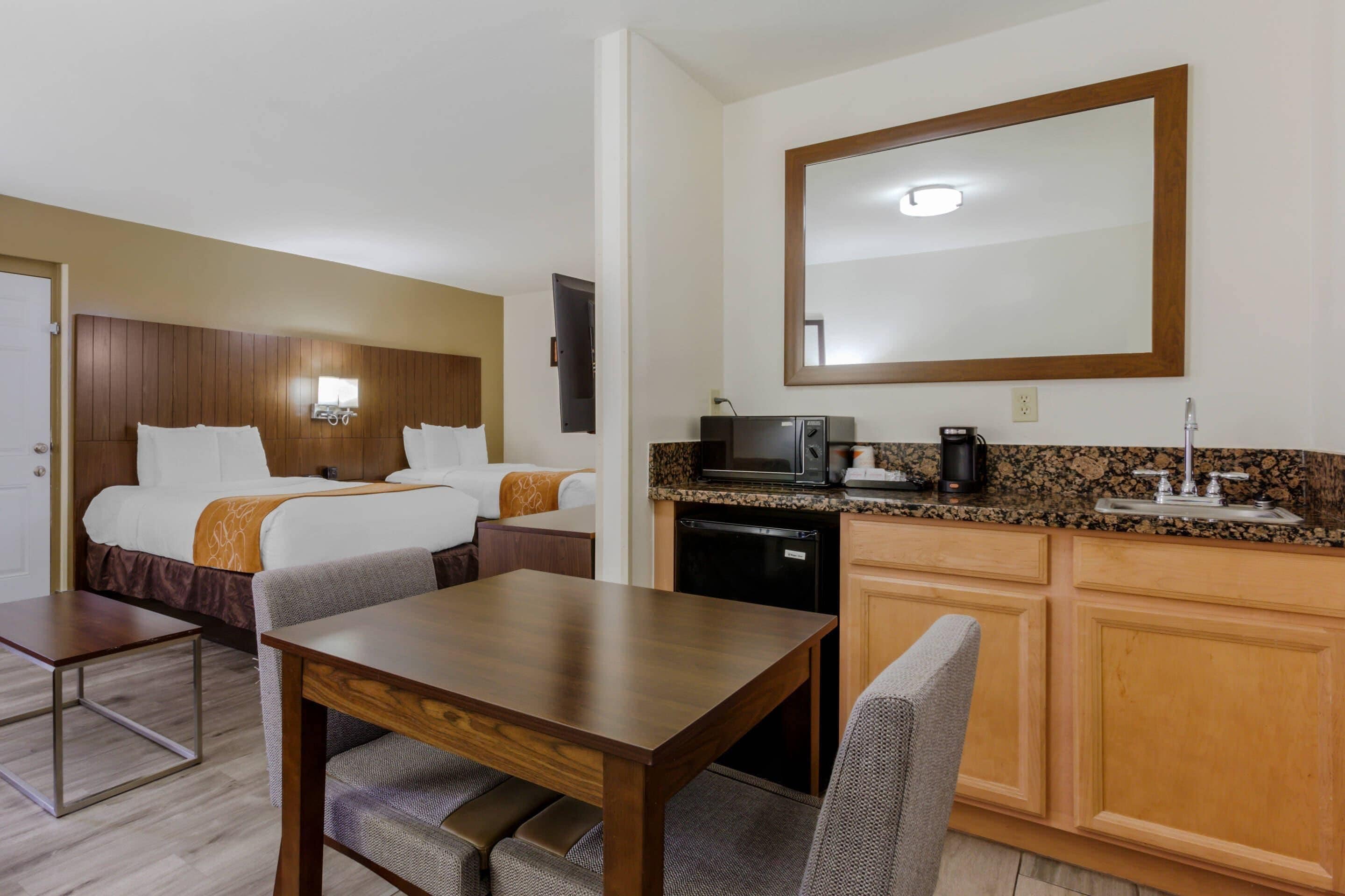 A hotel room with a bed, a dining table, a kitchen area with a microwave, and a large mirror.