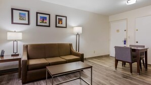 A furnished room with a sofa, a coffee table, a desk with a lamp, a dining table with chairs, and framed pictures on the wall. - Comfort Suites Tucson near Sabino Canyon (Tucson)