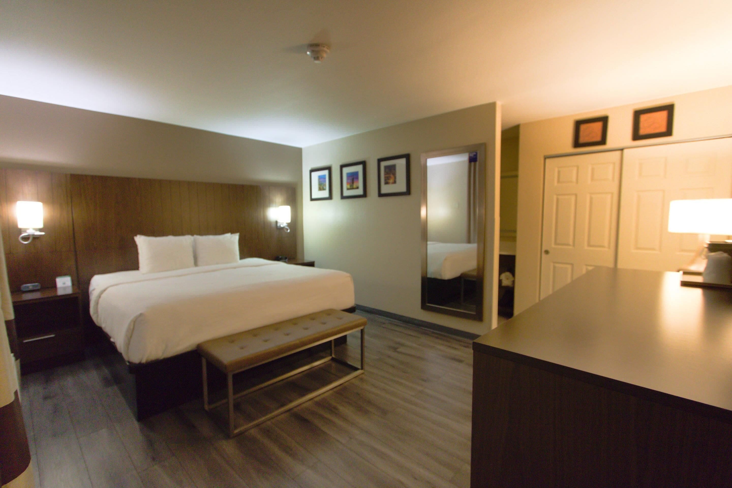 Een hotelkamer met een bed, nachtkastjes, een bankje, een spiegel en een bureau met een lamp.
