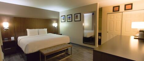 A hotel room with a bed, bedside tables, a bench, a mirror, and a desk with a lamp.