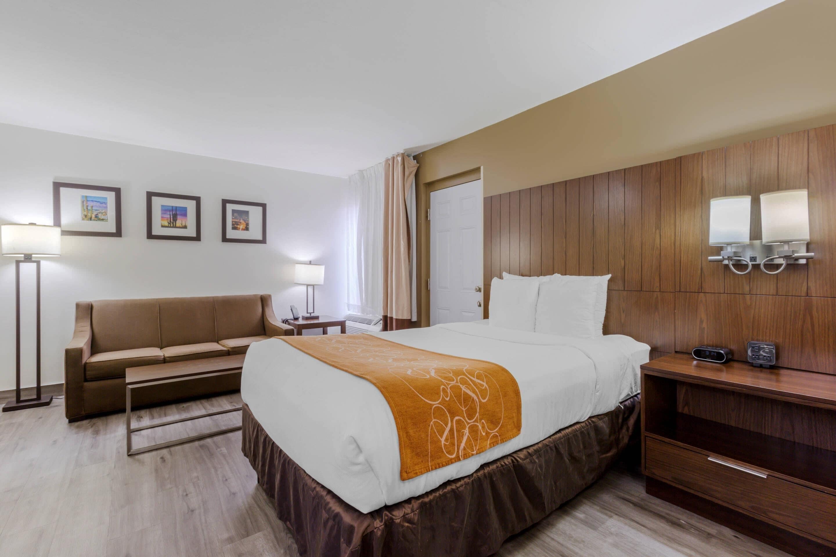 Habitación de hotel con cama, sofá, mesita de noche, lámpara y cuadros en la pared.