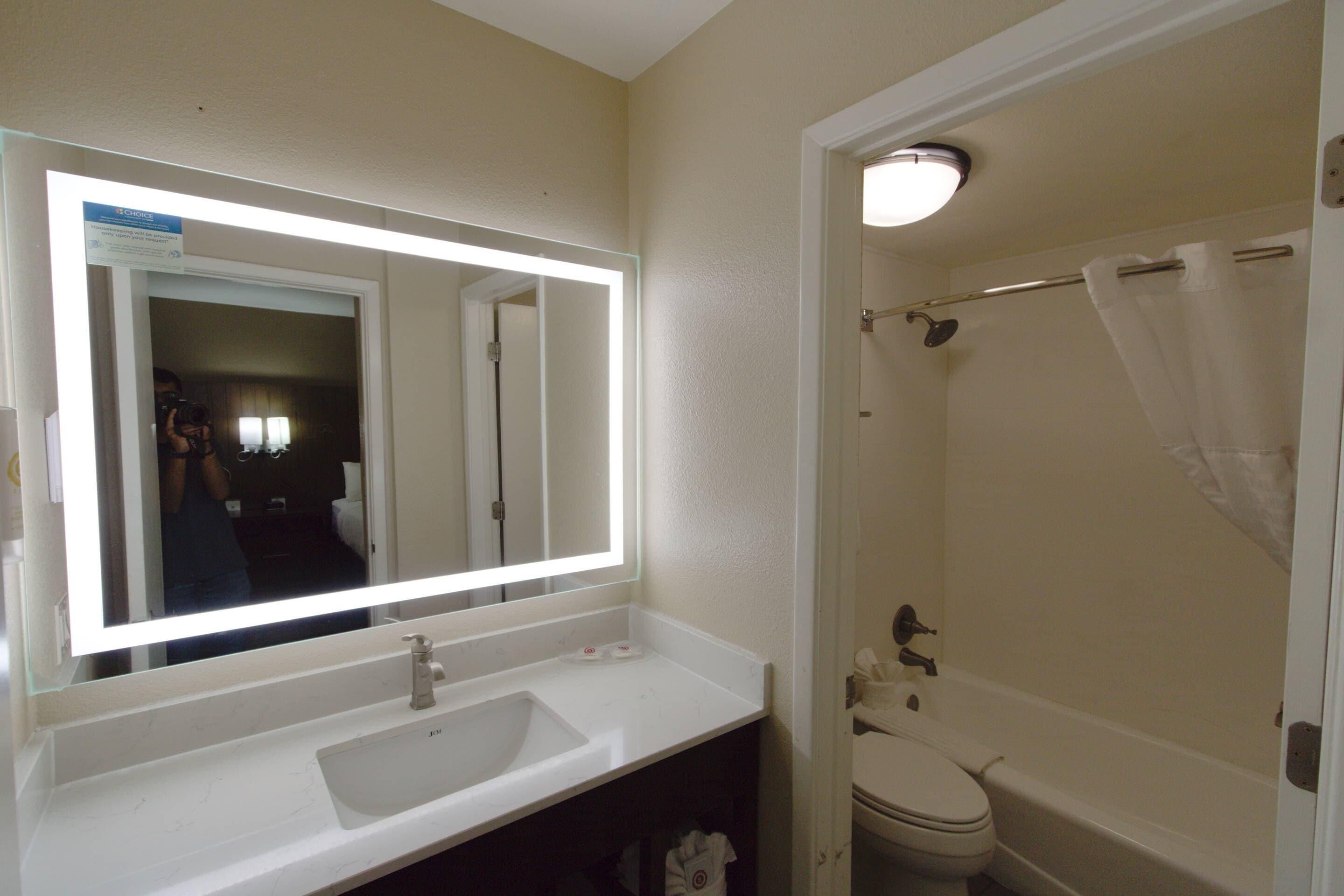 Une salle de bain avec un lavabo blanc, un miroir avec un éclairage intégré, des toilettes et un rideau de douche.