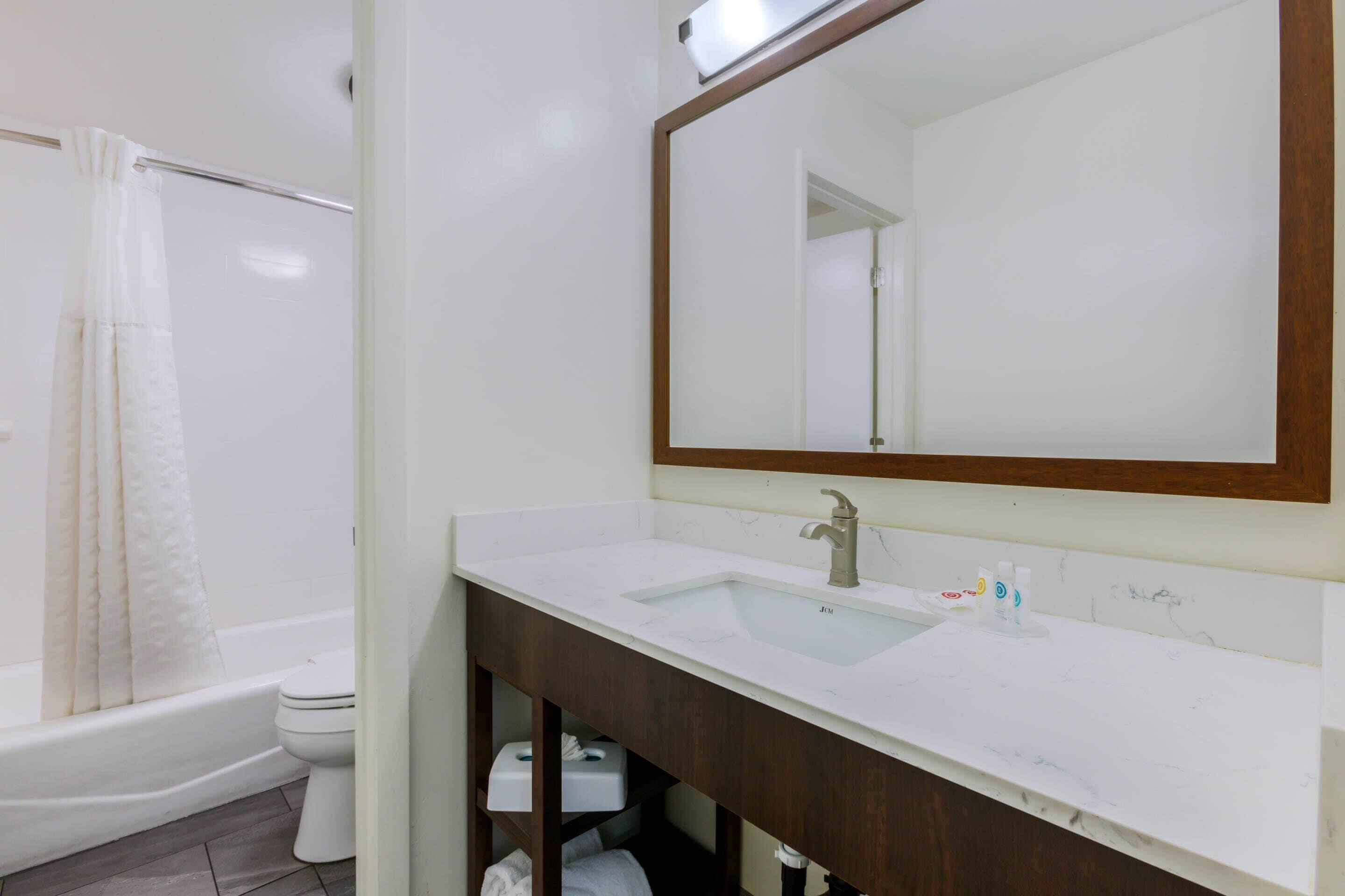 Un baño con lavamanos blanco, espejo, bañera y retrete.